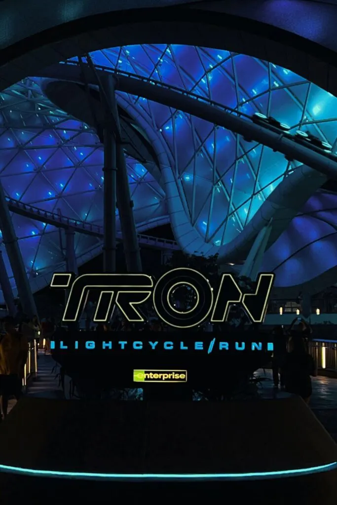 Photo of the entrance to TRON Lightcycle Run roller coaster at night with a line of lightcycles going by on the track.