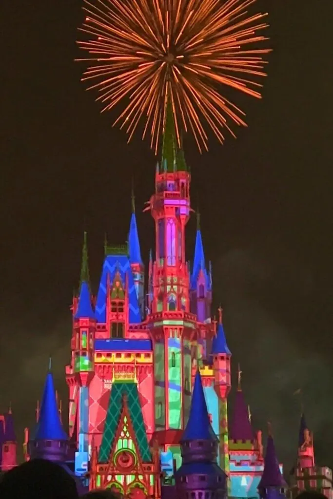 Photo of Cinderella Castle with Christmas laser projections at night and red fireworks bursting overhead.