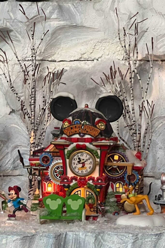 Photo of part of the Christmas village at Disney's Yacht Club, featuring the Mickey Mouse Watch Factory building and figurines of Mickey Mouse and Pluto.