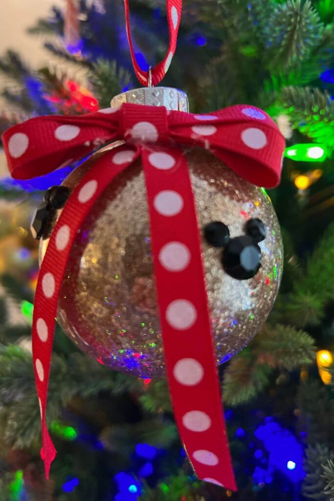 Closeup of a gold glittered ornament with black rhinestone Mickey Mouse heads and a red polka dot bow.