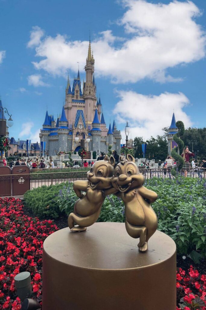 Photo of the golden Chip & Dale statue with red flowers in the foreground and Cinderella Castle in the background.