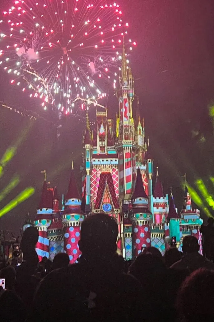 Photo of red and green lights projected on Cinderella Castle with red fireworks bursting in the sky at Magic Kingdom.