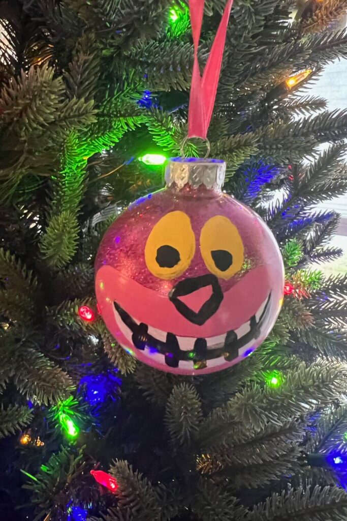 Closeup of a handmade Cheshire Cat ornament with a dark pink glittery base.