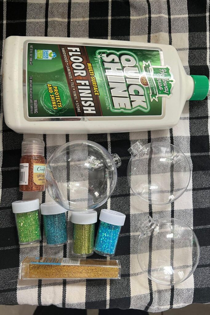 Flat lay photo of supplies for DIY glitter ornaments: a bottle of quick shine floor finish, clear plastic ornaments, and various colors of glitter.
