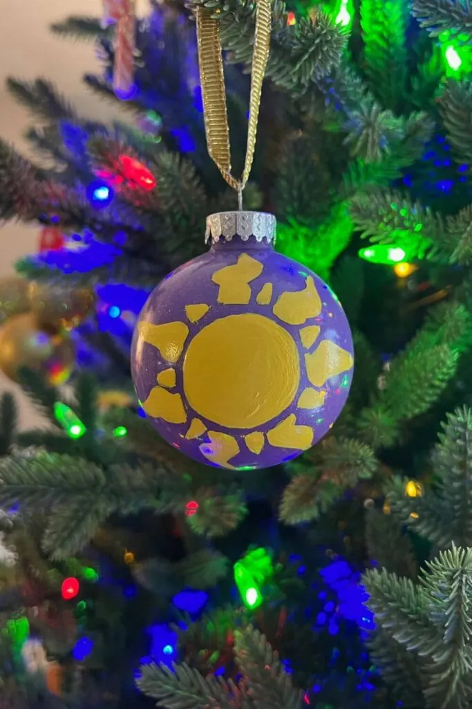 Closeup of a purple handpainted ornament with the yellow Tangled sun icon in the middle