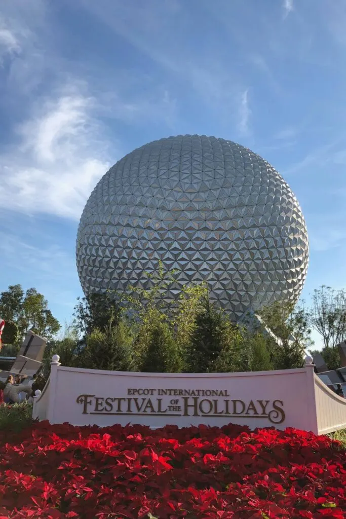 Photo of Spaceship Earth with a sign for Epcot International Festival of the Holidays and red flowers in the foreground.