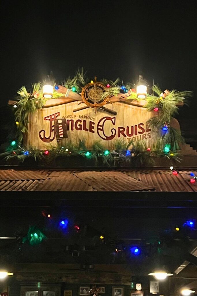 Closeup of the signage for Jingle Cruise at night, with colorful Christmas lights wrapped around it.