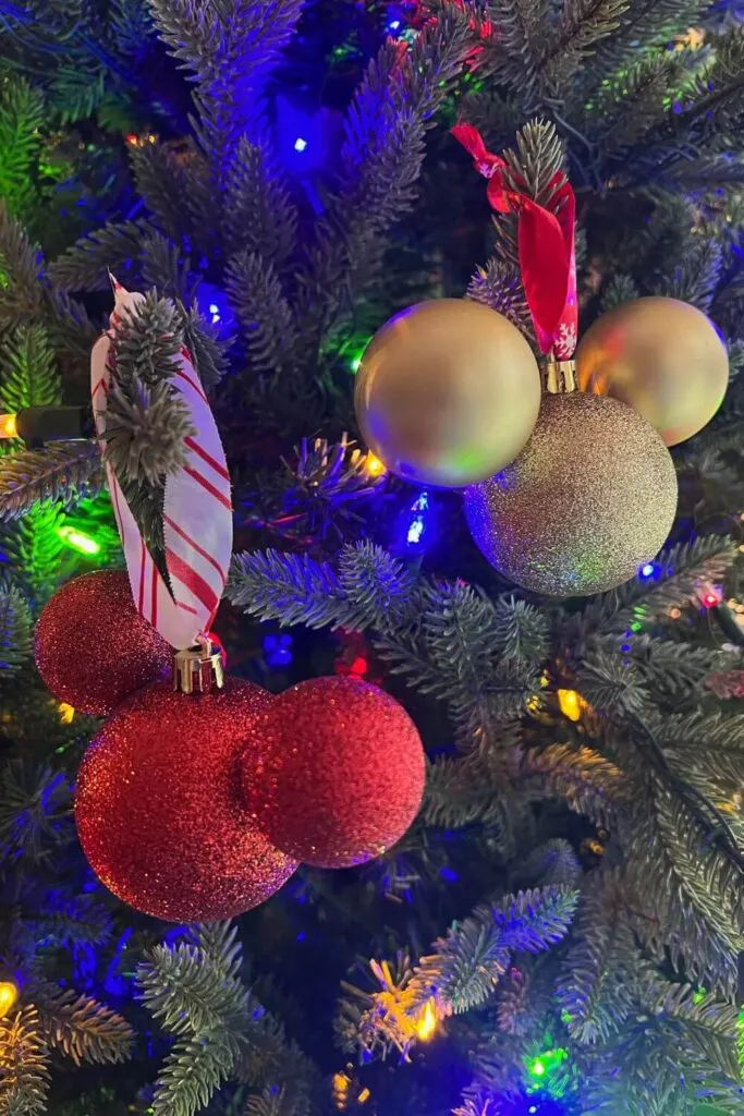 Closeup photo of two Mickey Mouse shaped Christmas ornaments hanging on a tree, one red and one gold.