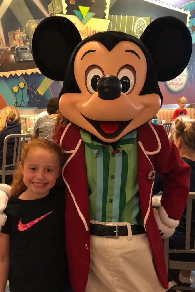 Photo of a young girl posing with Mickey Mouse in his Christmas blazer.