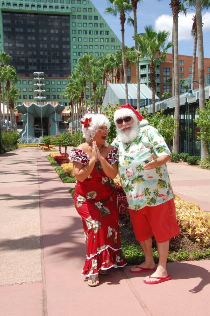 Photo of Mrs. Claus and Santa in tropical outfits, posing outside the Walt Disney World Swan & Dolphin hotel.