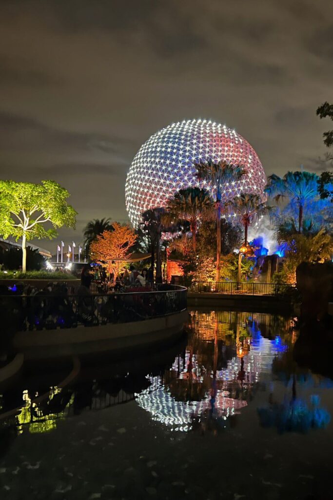 Photo of Spaceship Earth at night, reflecting in nearby water.