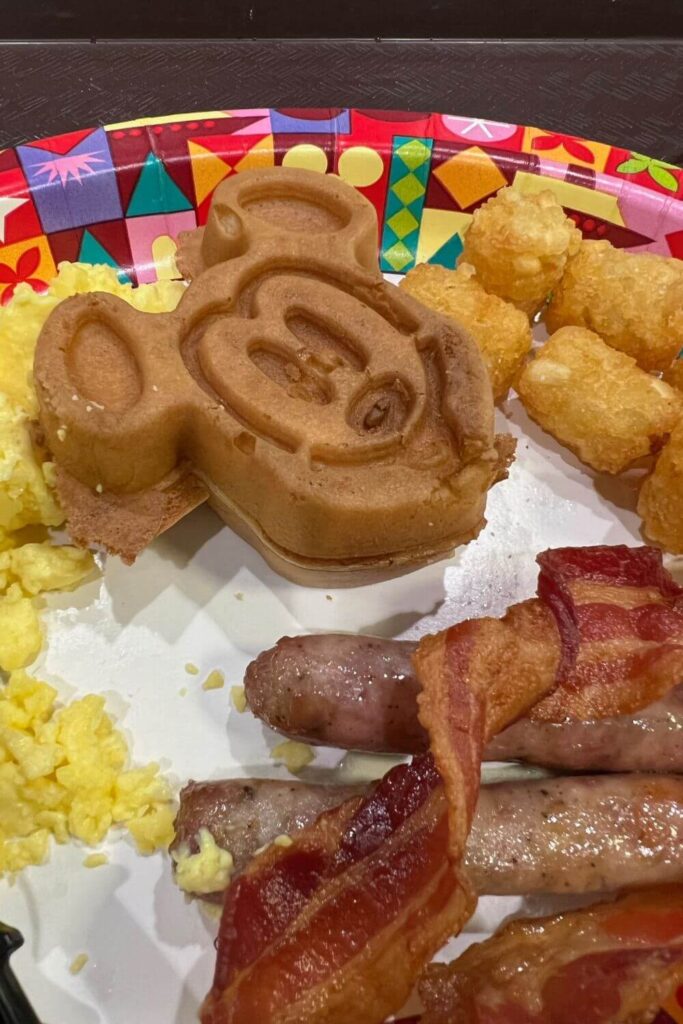 Closeup of a classic breakfast plate at Disney World with a Mickey waffle, eggs, tots, sausage, and bacon.