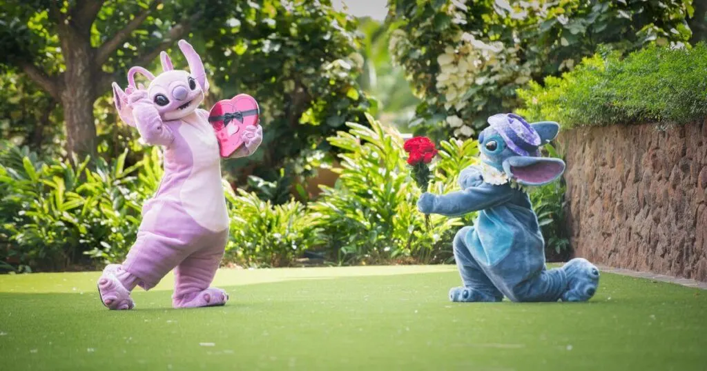 Photo of Stitch on one knee, holding flowers out at Angel, who's holding a heart-shaped box of chocolates while posing shyly.