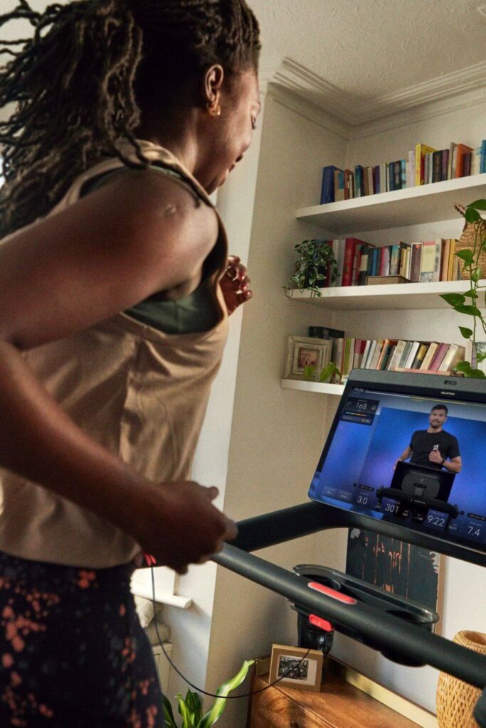 Photo of a black woman running on a Peloton treadmill at home.