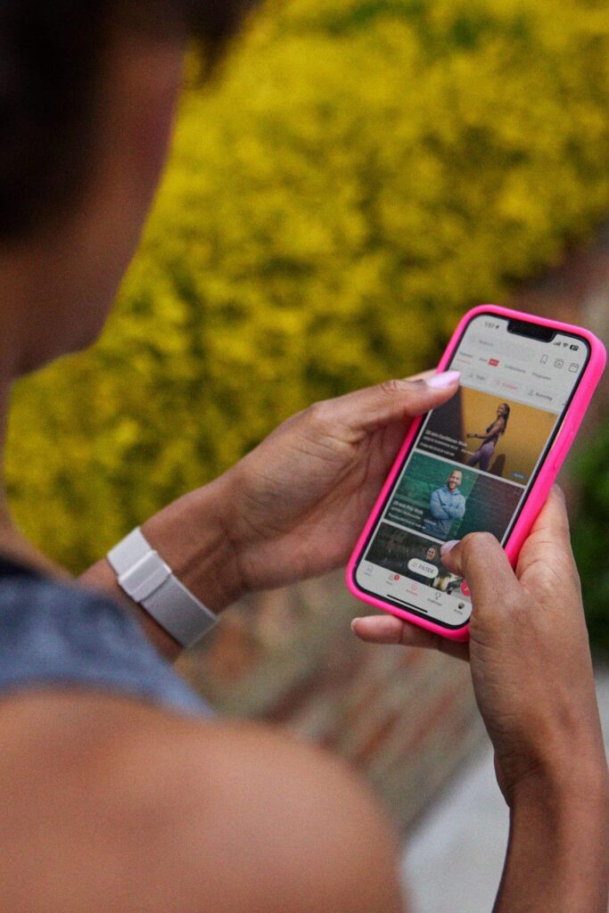 Photo looking over a woman's shoulder looking at the Peloton app on a mobile phone.