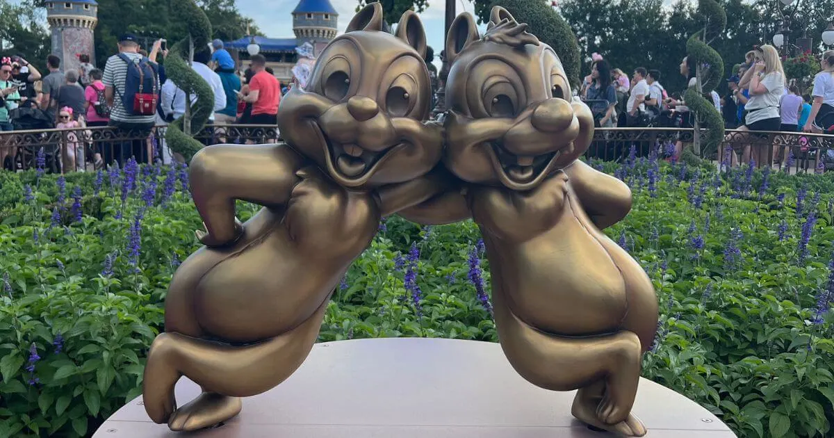 Closeup photo of golden Chip & Dale statues at Disney World with flowers behind them.