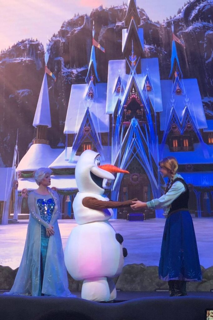 Photo of Anna and Olaf holding hands while Elsa looks on during the Frozen Sing-Along show at Hollywood Studios.