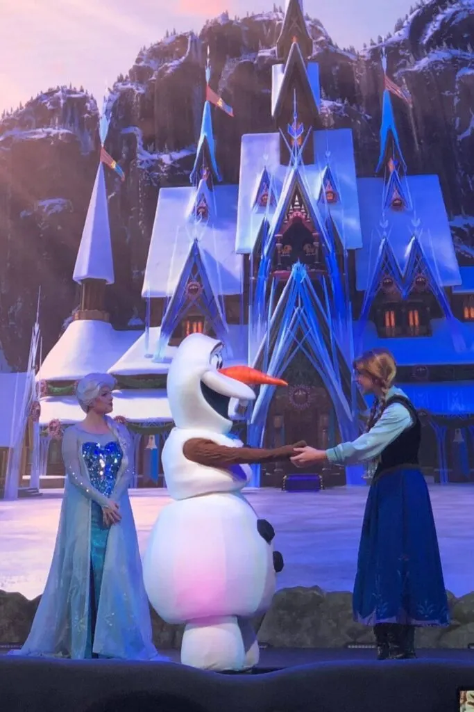 Photo of Anna and Olaf holding hands while Elsa looks on during the Frozen Sing-Along show at Hollywood Studios.