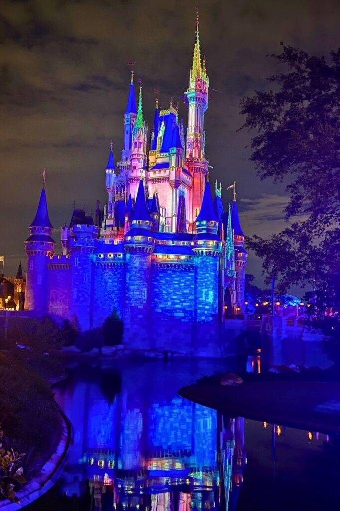 Photo of Cinderella Castle at night with laser projections on it, as it reflects in the moat in front of it.
