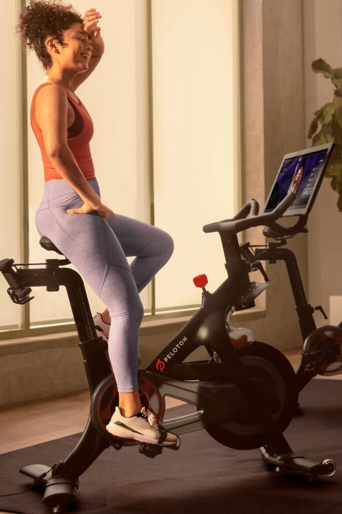 Photo of a woman wiping sweat off her forehead after finishing a Peloton ride on a bike at a hotel fitness cente.r