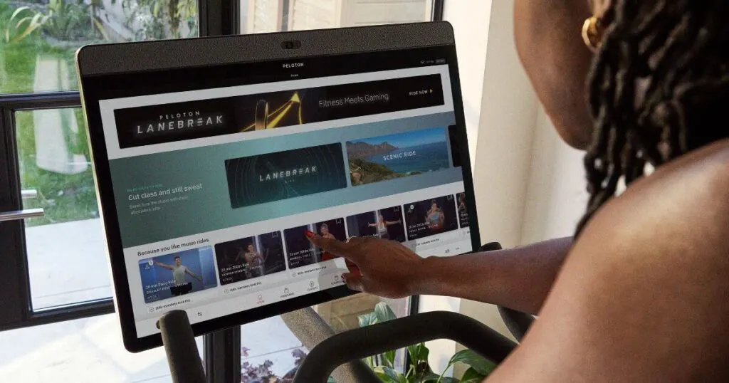 Photo of a black woman browsing classes on the Peloton bike interface.