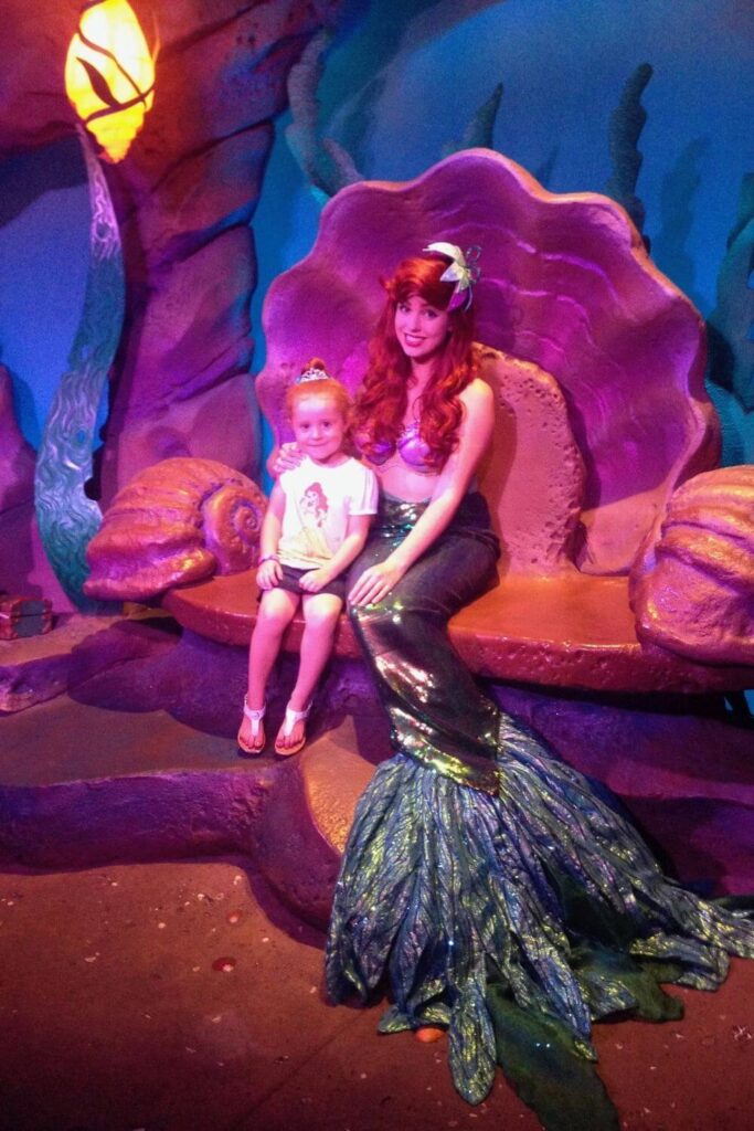 Photo of a young girl sitting for a photo with Ariel in mermaid form.