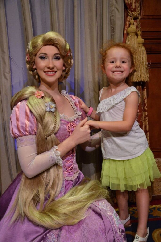 Photo of a young girl with a big smile, posing with Rapunzel.