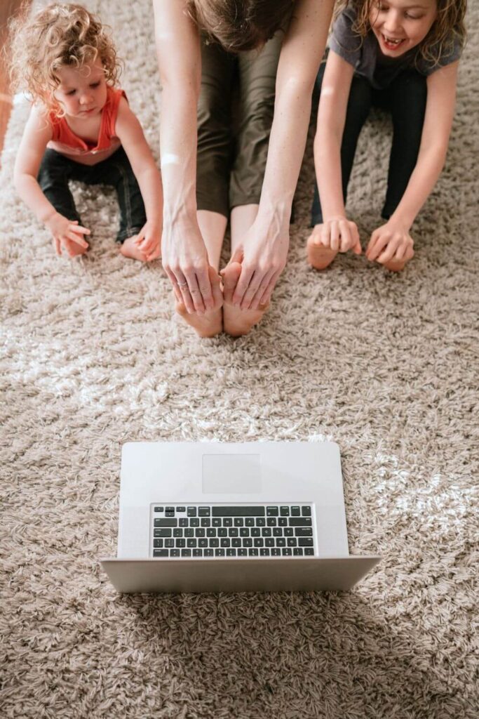 Photo of an adult flanked by two young kids, as they all stretch while watching a workout classes on a laptop.