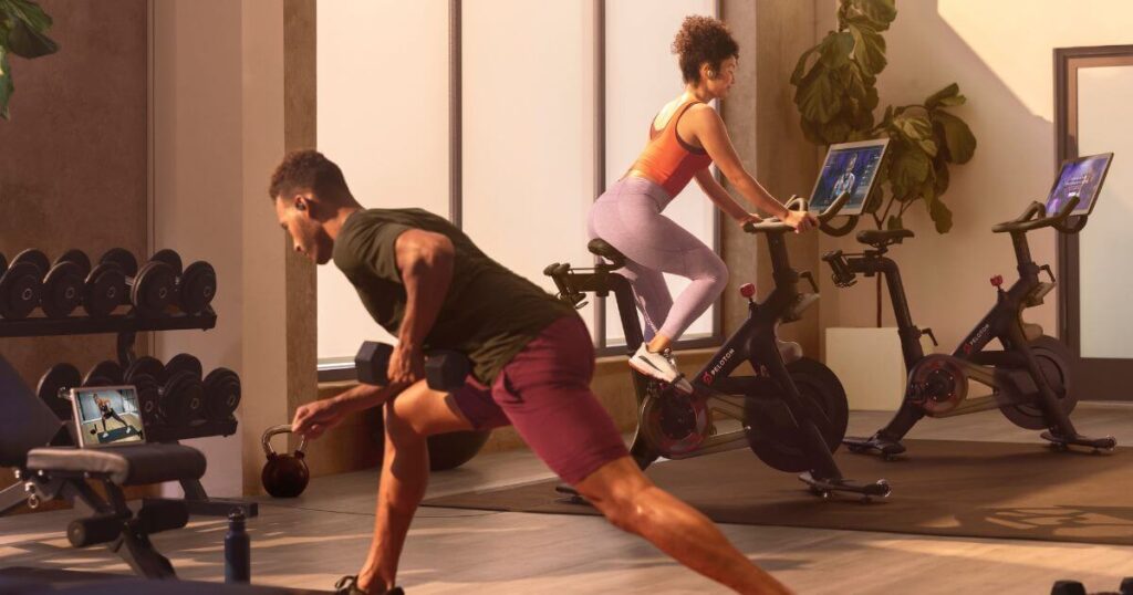 Photo of a man doing a strength workout with the Peloton app and a woman doing a Peloton ride at a hotel gym.