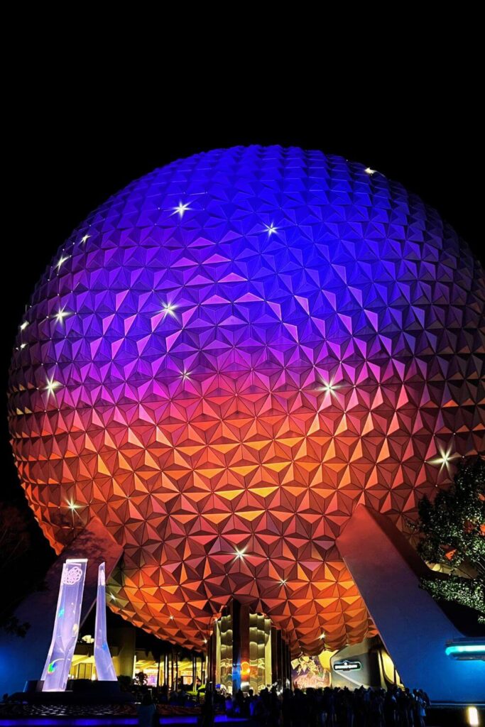 Photo of Spaceship Earth at night, lit up in blue, purple, fuchsia, and orange, with sparkling lights.