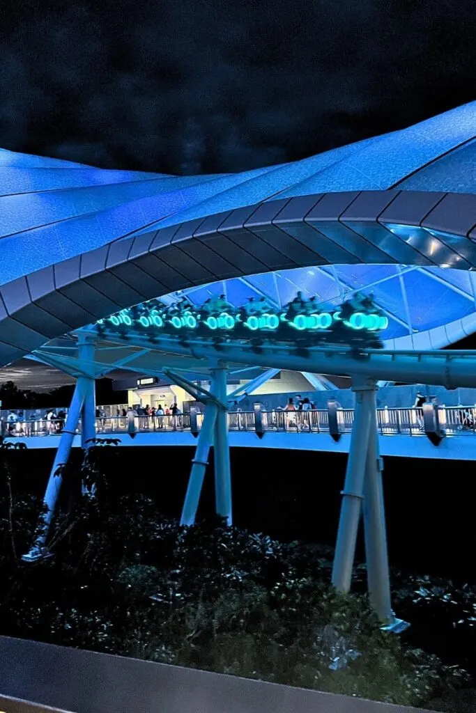 Photo of the TRON Lightcycle Run roller coaster speeding by at night, all lit up in neon blue.