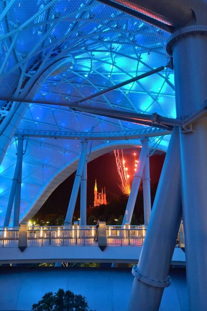 Photo looking through an opening in the TRON canopy with fireworks bursting and Cinderella Castle in the background.