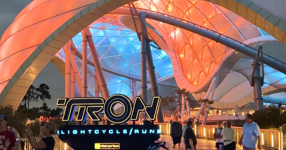 Horizontal photo of the entrance to TRON Lightcycle Run at Magic Kingdom in Disney World. The canopy above the roller coaster is a mix of neon blue and orange lights.