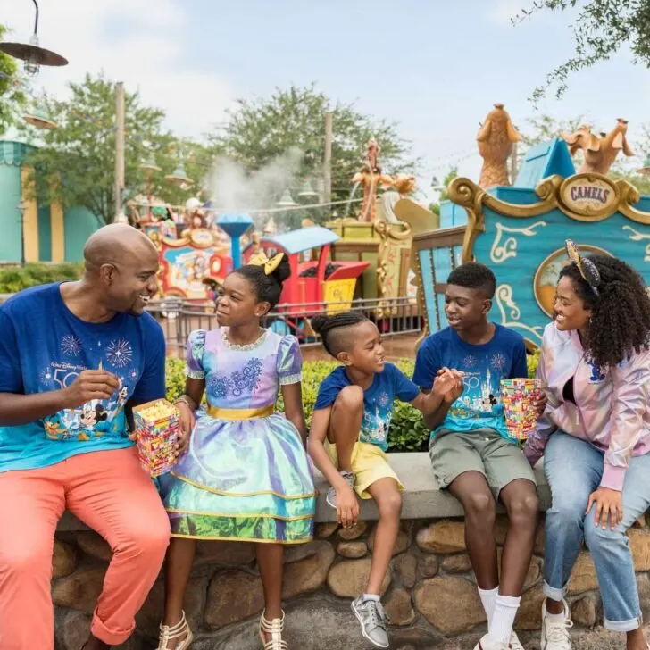 Photo of a mom and dad with 3 kids, enjoying popcorn at Magic Kingdom.