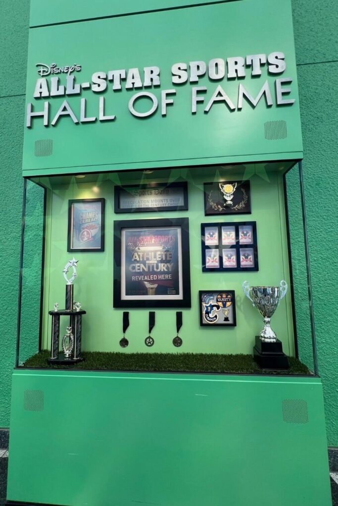 Photo of a large green display case with trophies, medals, and photos. A sign above it reads: Disney's All-Star Sports Hall of Fame.