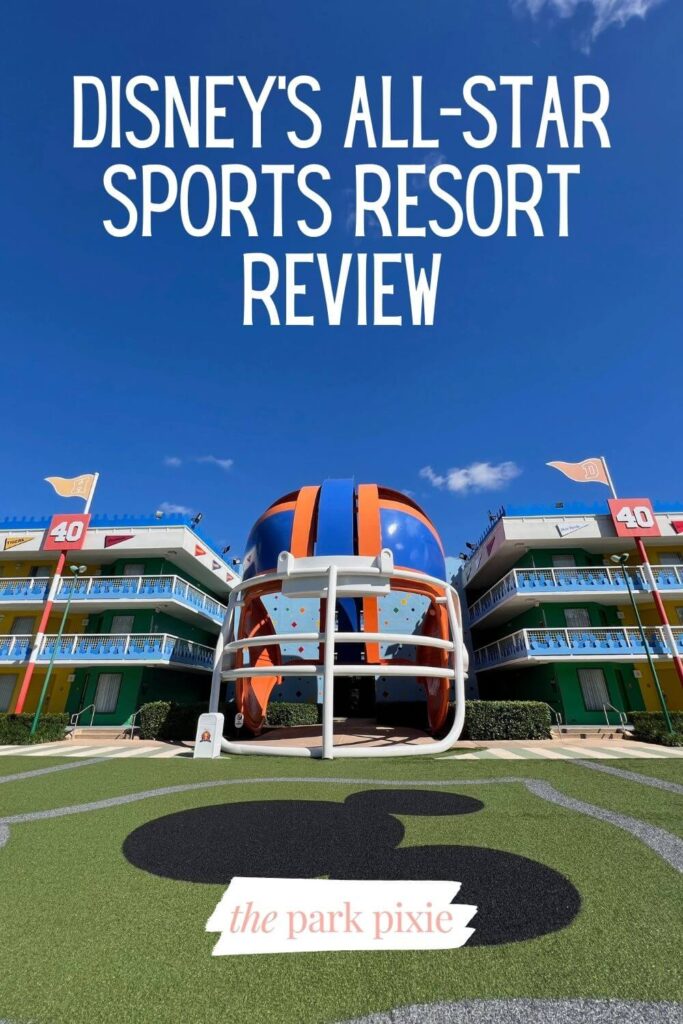 Vertical photo of a 3-story blue and orange football helmet nestled between two hotel buildings. In the foreground is a faux football field with a large Mickey Mouse head painted in the middle. Text overlay reads: Disney's All-Star Sports Resort Review.