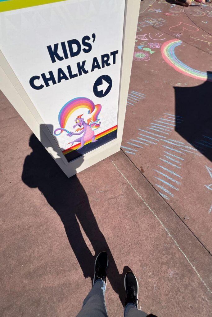 Photo of a placard that says "Kids' Chalk Art" with a photo of Figment, along with chalk drawings on the sidewalk.
