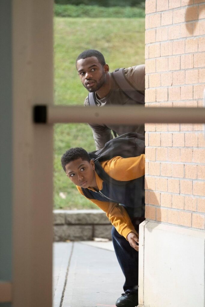 Photo still from the Disney+ movie, Safety, featuring Ray and Fahmarr peaking around a corner of a building.
