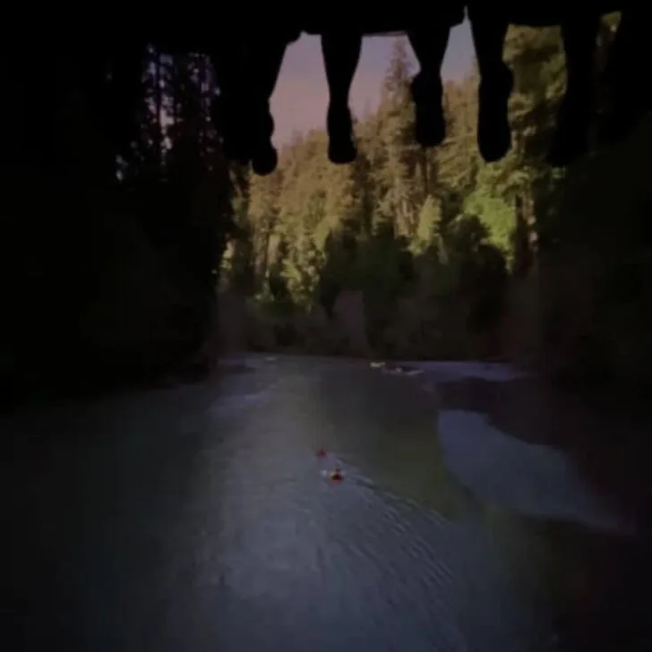 Photo of feet dangling above with a screen playing a scene through a river in Soarin' Over California.