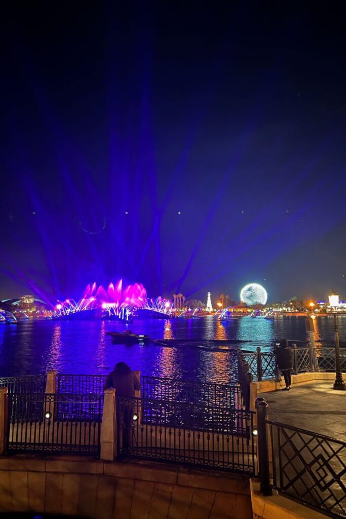 Photo of the World Showcase Lagoon at the end of the Luminous nighttime show at Epcot, with Spaceship Earth and the show's barges lit up.