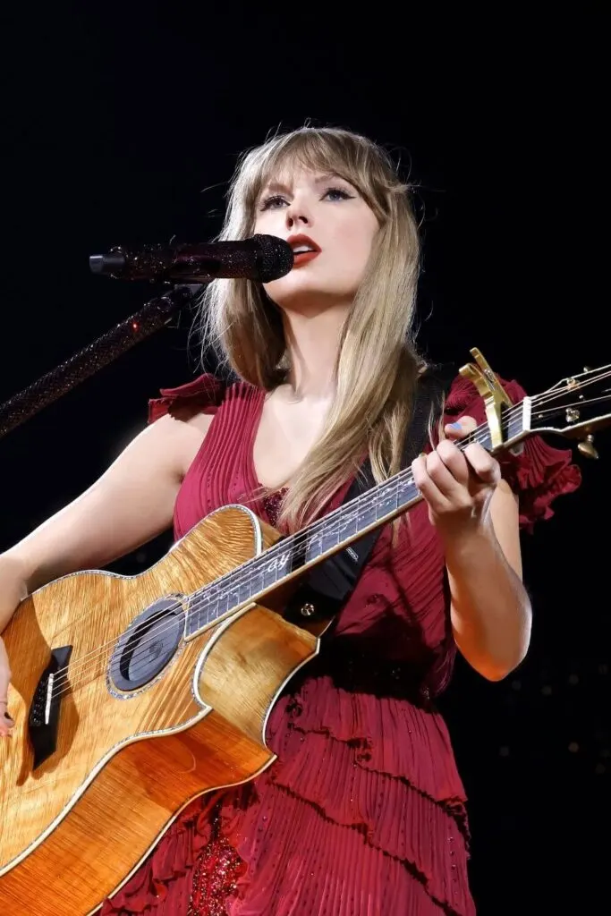 Closeup of Taylor Swift performing an acoustic set in a red pleated, ruffly dress during the Eras Tour.