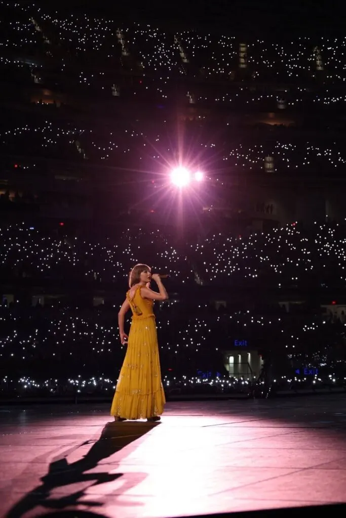 Photo of Taylor Swift performing a song from her Folklore album with star-like lights from the audience behind her.