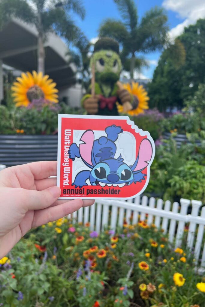 Closeup of a Walt Disney World annual passholder magnet featuring Stitch with an Epcot topiary in the background.