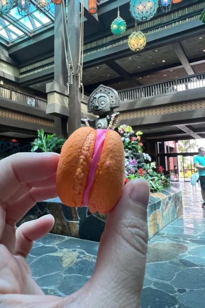 Closeup photo of a POG macaron with the Polynesian resort lobby in the background.