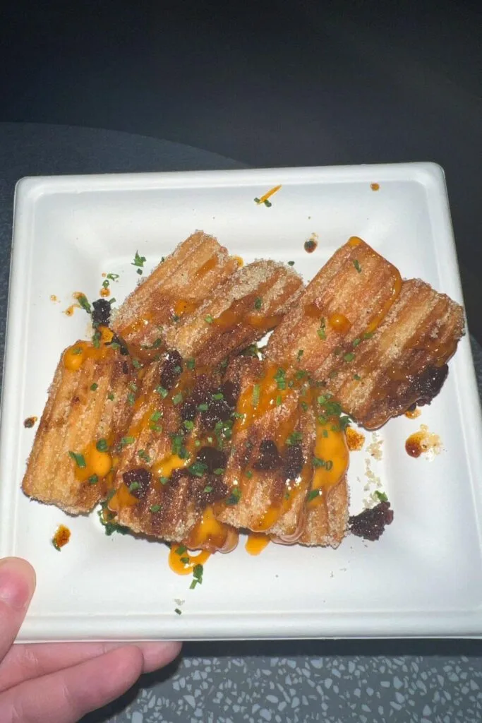 Photo of a plate of mini churros topped with chipotle aioli, candied bacon, and scallions.