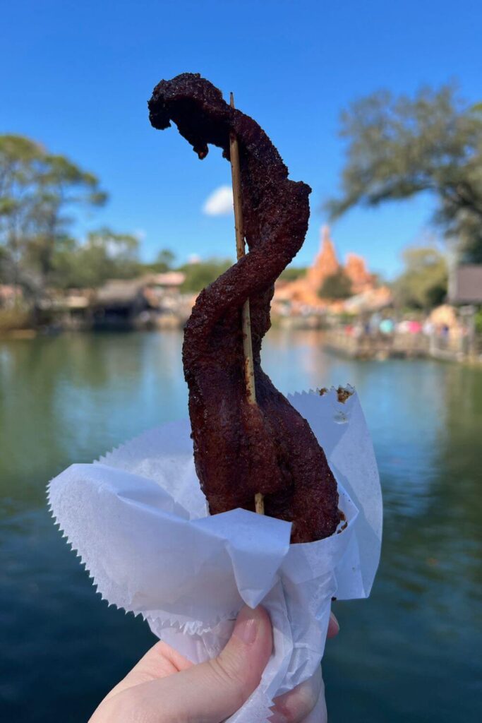 Photo of candied bacon on a stick with Big Thunder Mountain Railroad roller coaster in the background.