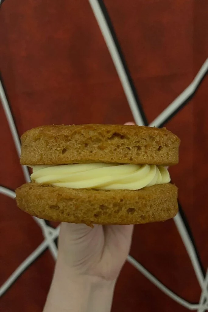 Photo of a carrot cake cookie with 2 thick slabs of carrot cake with buttercream in the middle.