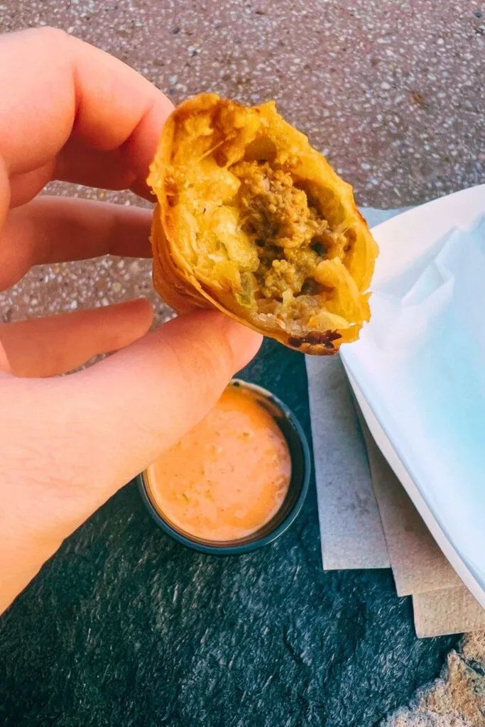 Closeup of a cheeseburger spring roll cut in half, with burger dip below it.