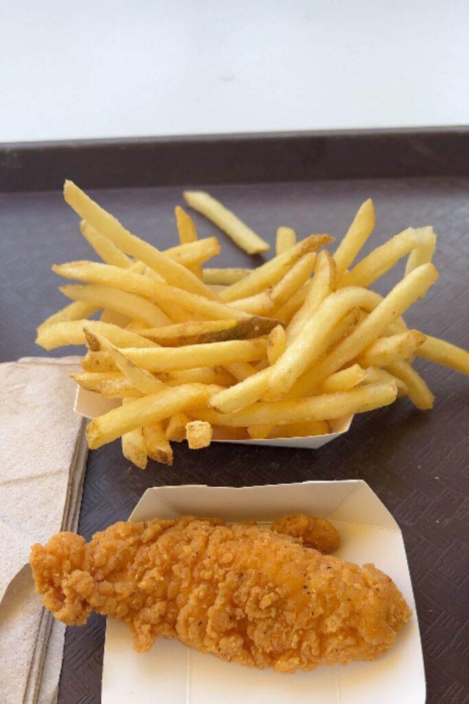 Photo of a crispy chicken tender and basket of french fries on a brown food tray.