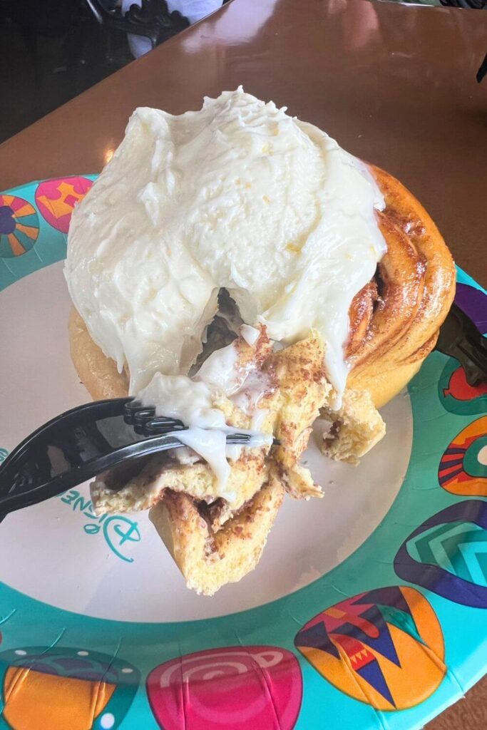 Photo of a giant cinnamon roll covered with a thick dollop of orange cream cheese icing.